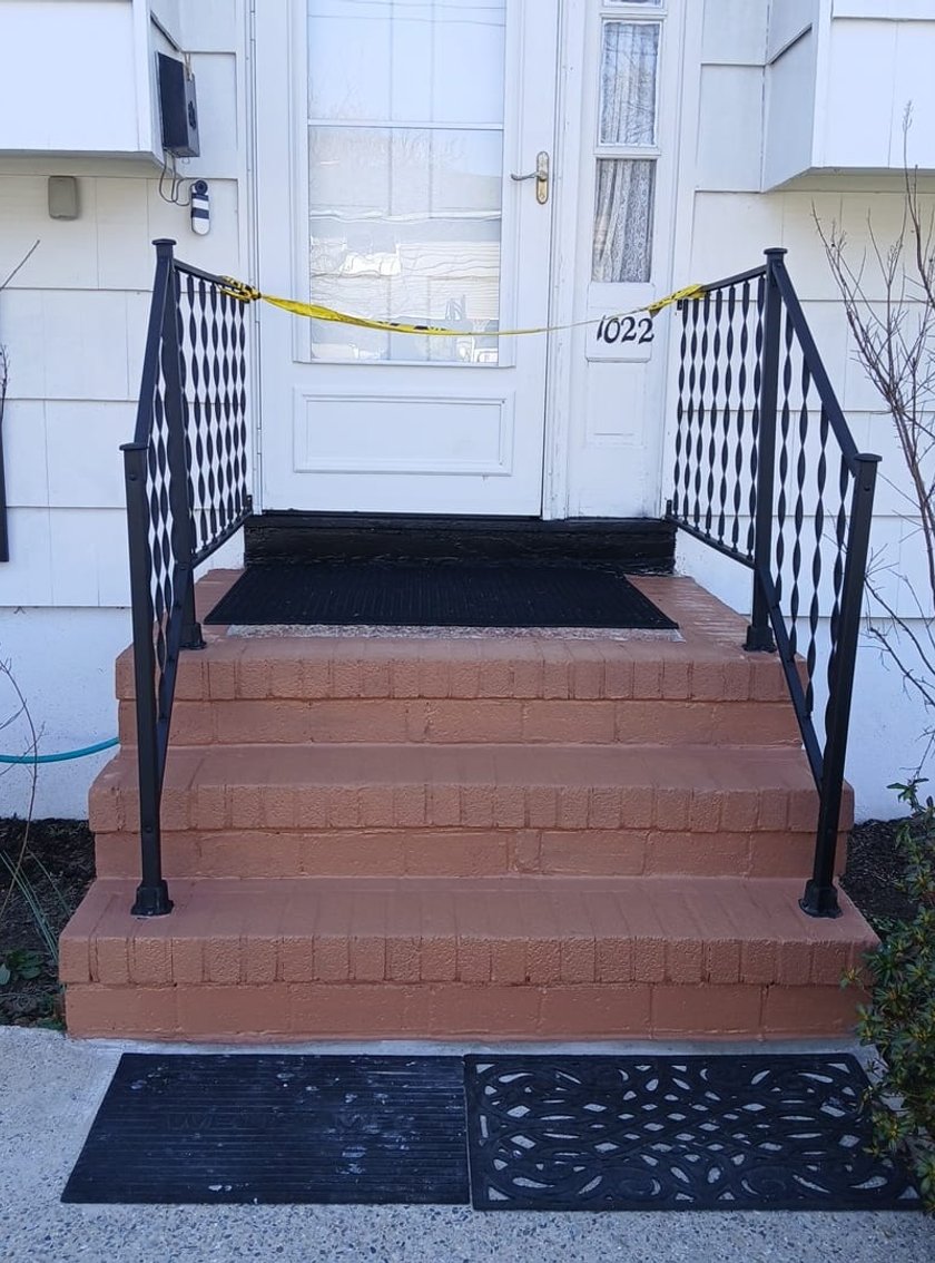 Front-on view of newly painted terracotta concrete steps with black wrought-iron railings leading to a white front door