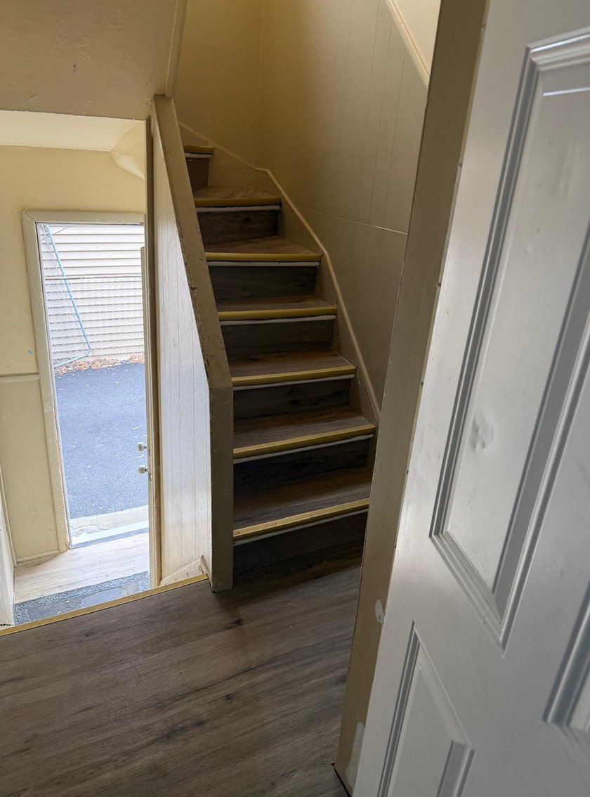 Interior stairwell with new wood-look vinyl plank treads and freshly painted walls leading down to a back-entry door