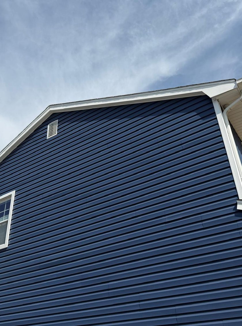 Side gable of a two-story home showing the full navy blue siding installation against blue sky