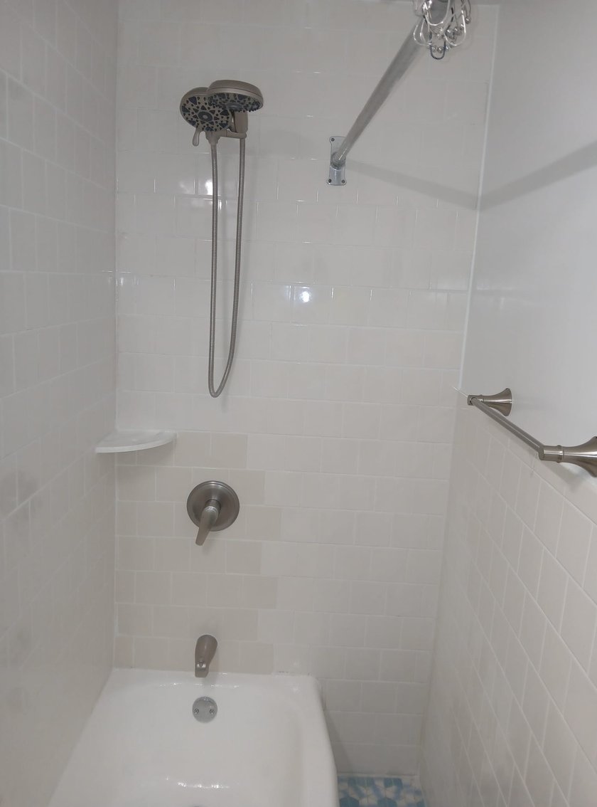 Tub and shower surround with white subway tile, brushed nickel handheld showerhead, tub spout, and corner soap shelf