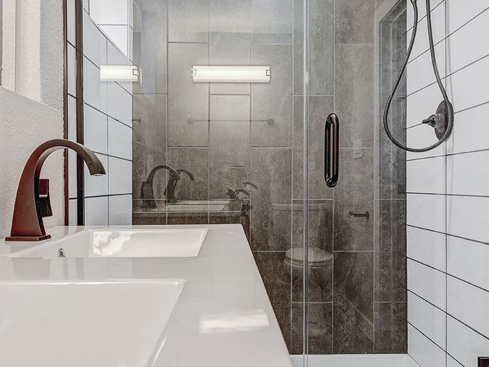 Bathroom with white subway-tile shower walls, glass enclosure, gray accent tile, and a double-sink vanity with bronze faucets
