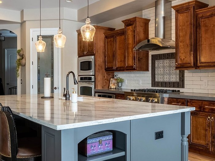 Kitchen with a freshly painted gray-blue island, warm wood perimeter cabinets, and three glass pendant lights