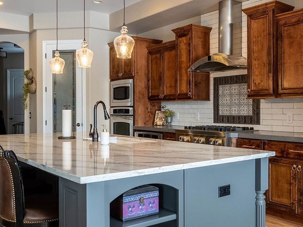 Kitchen with a freshly painted gray-blue island, warm wood perimeter cabinets, and three glass pendant lights
